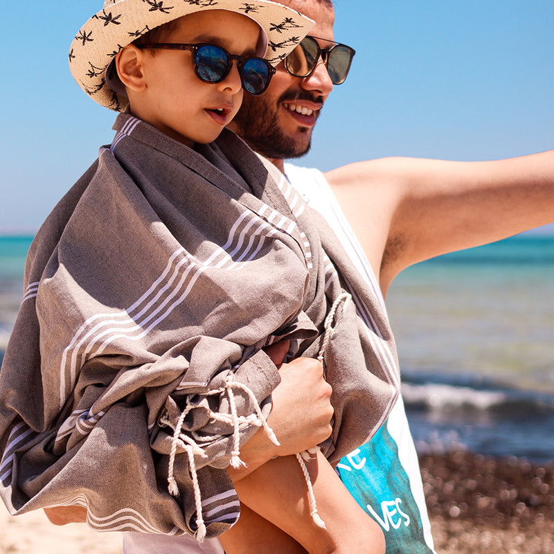 ein Kind in einer braunen Hamamtuch Fouta mit seinem Vater am Strand
