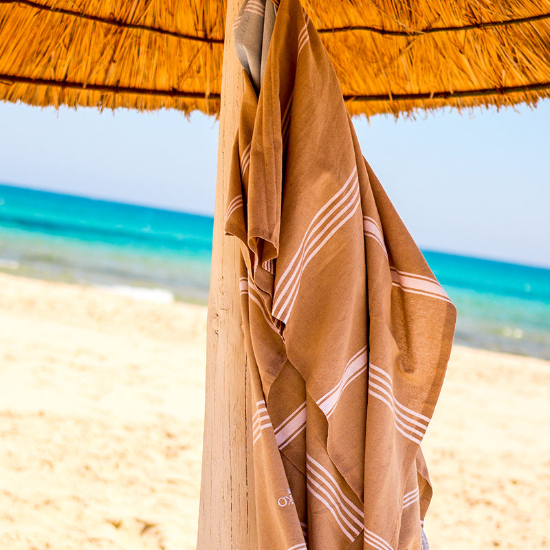 ein beiges Strandtuch, das an einem Sonnenschirm am Strand hängt