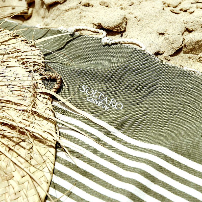 ein Hut auf einem khakifarbenen Strandtuch fouta das auf dem Sand liegt