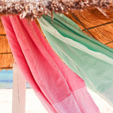 eine rosafarbene Fouta und ein aquablaues Strandtuch hingen unter dem Sonnenschirm 