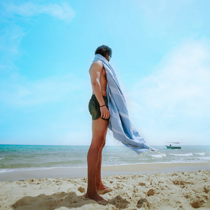 ein Mann am Strand mit einem hellblauen Hamamtuch auf den Schultern