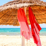 ein rosa Strandtuch und eine korallenrote Fouta hängen unter einem Sonnenschirm