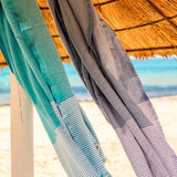 ein hellgraues Strandtuch und eine aquablaue Fouta unter dem Sonnenschirm