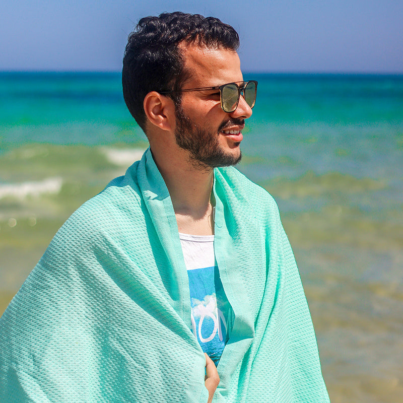 Mann mit Sonnenbrille am Strand mit aquablauem Hamamtuch
