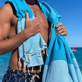 ein Mann am Strand mit blauem Strandtuch fouta auf den Schultern