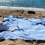 eine Strandtasche und Sonnencreme auf einem blauen Hamamtuch im Sand
