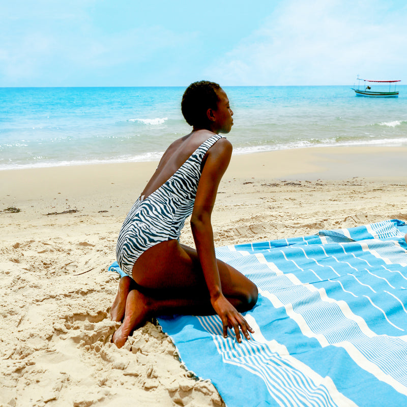 ein Mädchen am Strand das auf einem aquablauen Hamamtuch sitzt