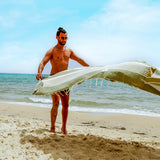 ein Mann am Strand der ein olivgrünes Strandtuch in den Sand legt