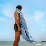 Mann am Strand mit einem blauen Strandtuch Saunatuch auf den Schultern