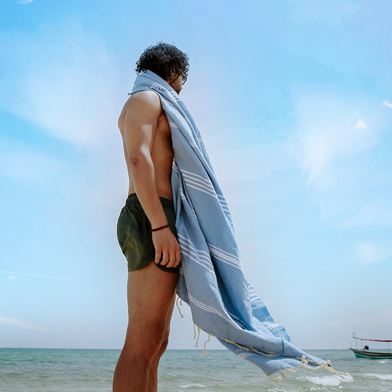 ein Mann am Strand mit jeansblauem Hamamtuch strandtuch auf den Schultern