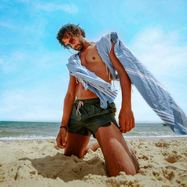 ein Mann am Strand mit einem hellblauen XXL Hamamtuch auf den Schultern