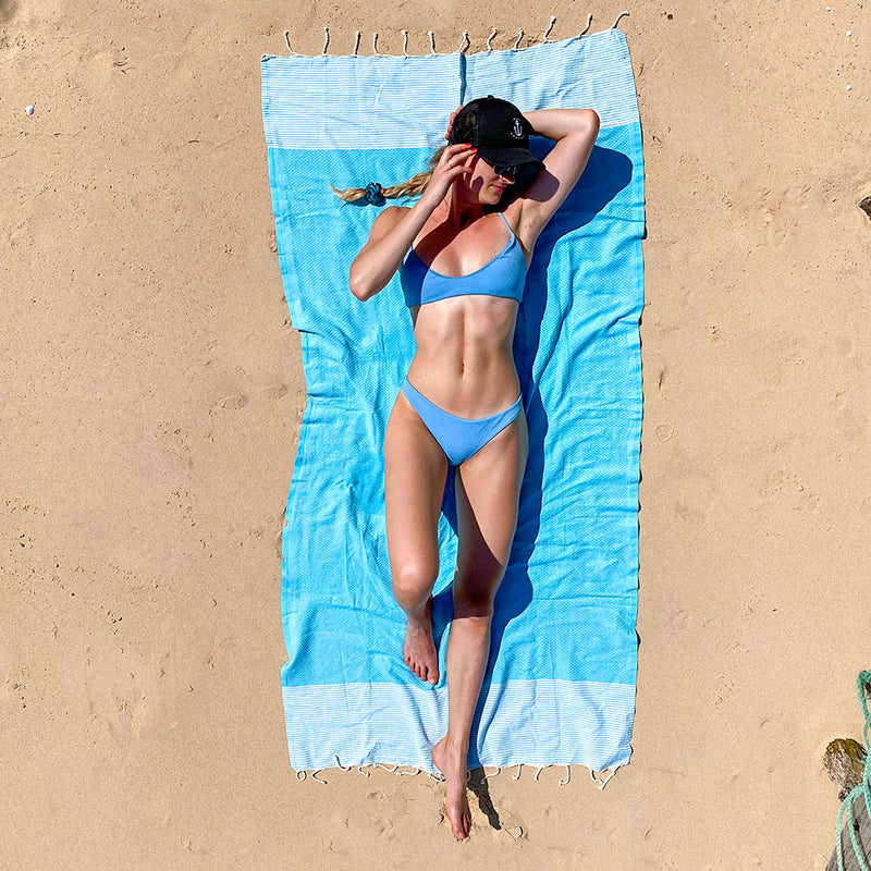 Mädchen im Bikini sonnt sich am Strand auf blauem Strandtuch Fouta