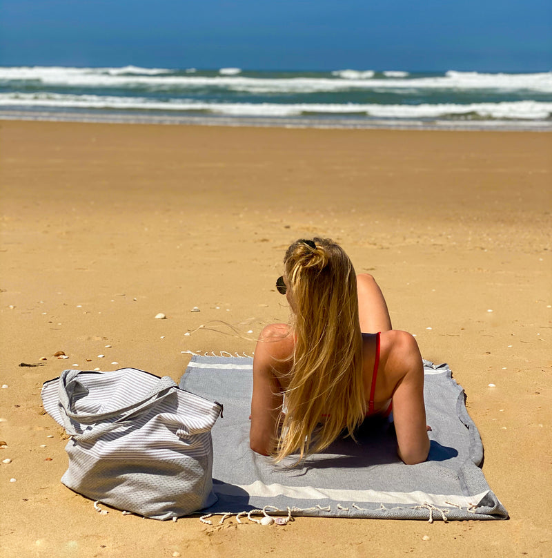 Mädchen mit einer Strandtasche auf einem khaki Strandtuch am Strand liegend