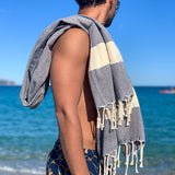 Mann am Strand mit anthrazitfarbenes Strandtuch auf der Schulter