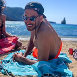 Mann am Strand auf einem aquablauen Strandtuch fouta liegend