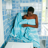 Frau wickelt sich im Badezimmer in ein aquablaues Hamamtuch fouta