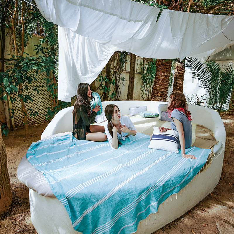 eine Gruppe von Mädchen die auf einem Bett mit einem aquablauen XXL hamamtuch im Freien faulenzen