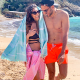 Mann hält eine Frau in einer rosa Fouta und einem aquablauen Strandtuch am Strand