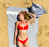 Frau am Strand auf einem hellgrauen Strandtuch und mit einer hellgrauen Strandtasche