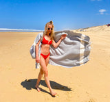 Frau im roten Bikini am Strand mit einem hellgrauen Strandtuch Fouta
