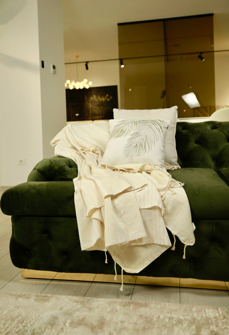 eine beigefarbene Decke mit Kissen auf einem grünen Sofa